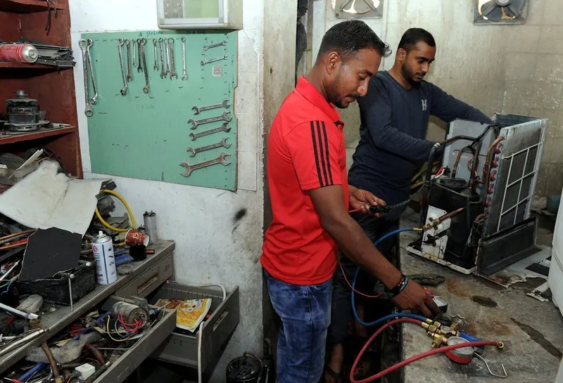 Two technicians repairing an AC outdoor unit in the workshop