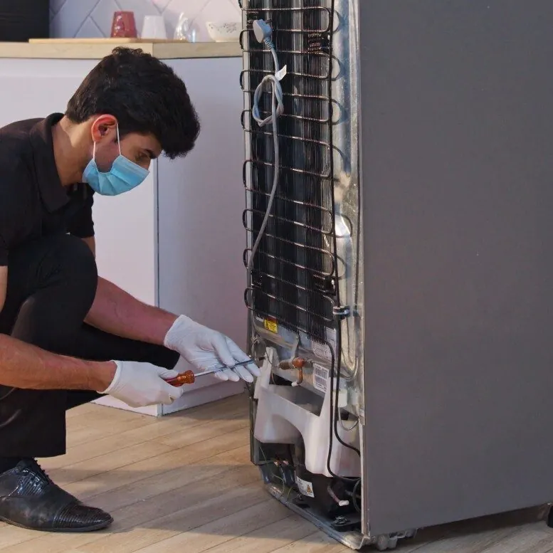 Technician repairing the back of a refrigerator at a home in Lahore