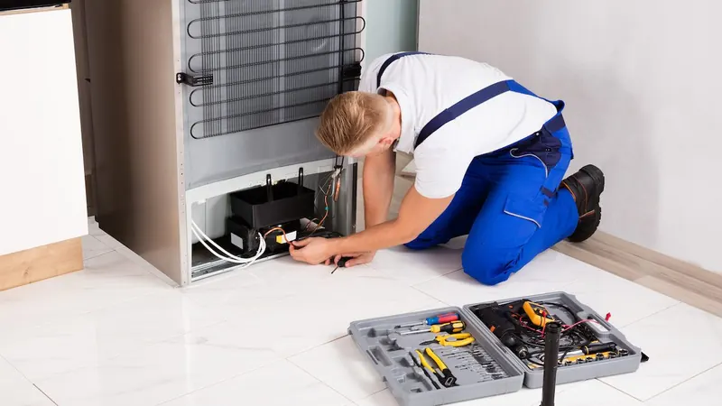 Technician repairing the compressor area at the back of a refrigerator